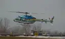 Ein blauer Hubschrauber mit Regenbogenstreifen hebt von einem Landeplatz ab
