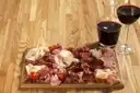 Ein Brett mit Wurst und Käse neben einem Glas Rotwein
