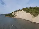 Die hellen Lehmklippen der Scarborough Bluffs ragen über das graublaue Wasser des Ontariosees, oben grüne Bäume.