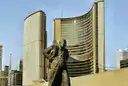 Die geschwungenen Türme des Rathauses von Toronto im Sonnenlicht, davor eine Bronzestatue, auf dem Nathan Phillips Square.