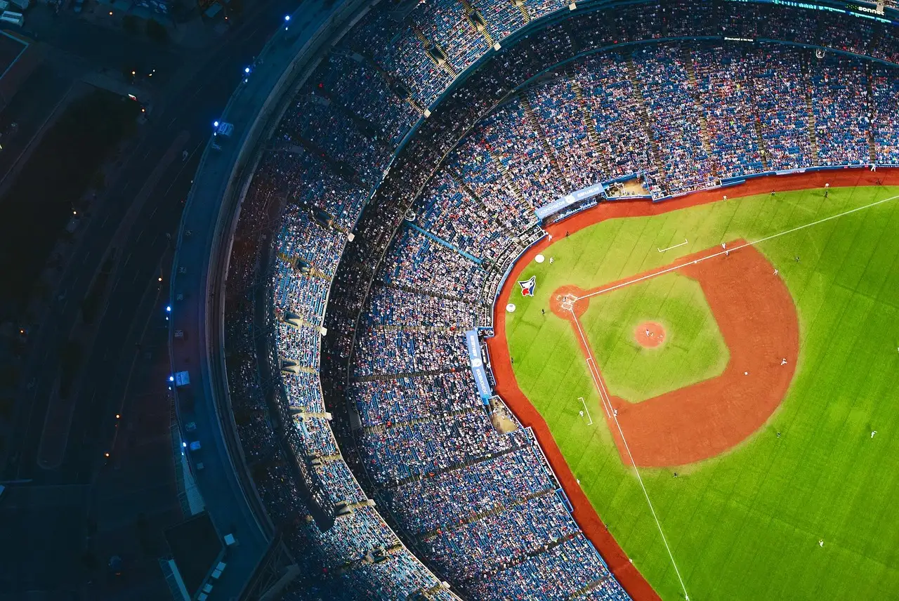 Blick von oben in ein volles Baseballstadion bei Nacht, mit Spielfeld, rotbraunem Infield und dicht besetzten Rängen.
