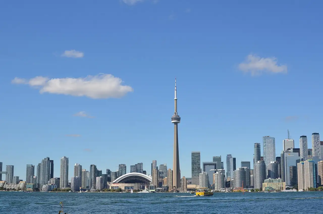 Der CN Tower und Torontos Skyline über den Ontariosee an einem sonnigen Tag, mit einem kleinen Boot auf dem Wasser