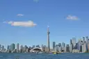 Der CN Tower und Torontos Skyline über den Ontariosee an einem sonnigen Tag, mit einem kleinen Boot auf dem Wasser