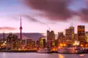 Der CN Tower und Downtown Toronto in der Dämmerung, mit zwei weißen Ausflugsbooten im Hafen