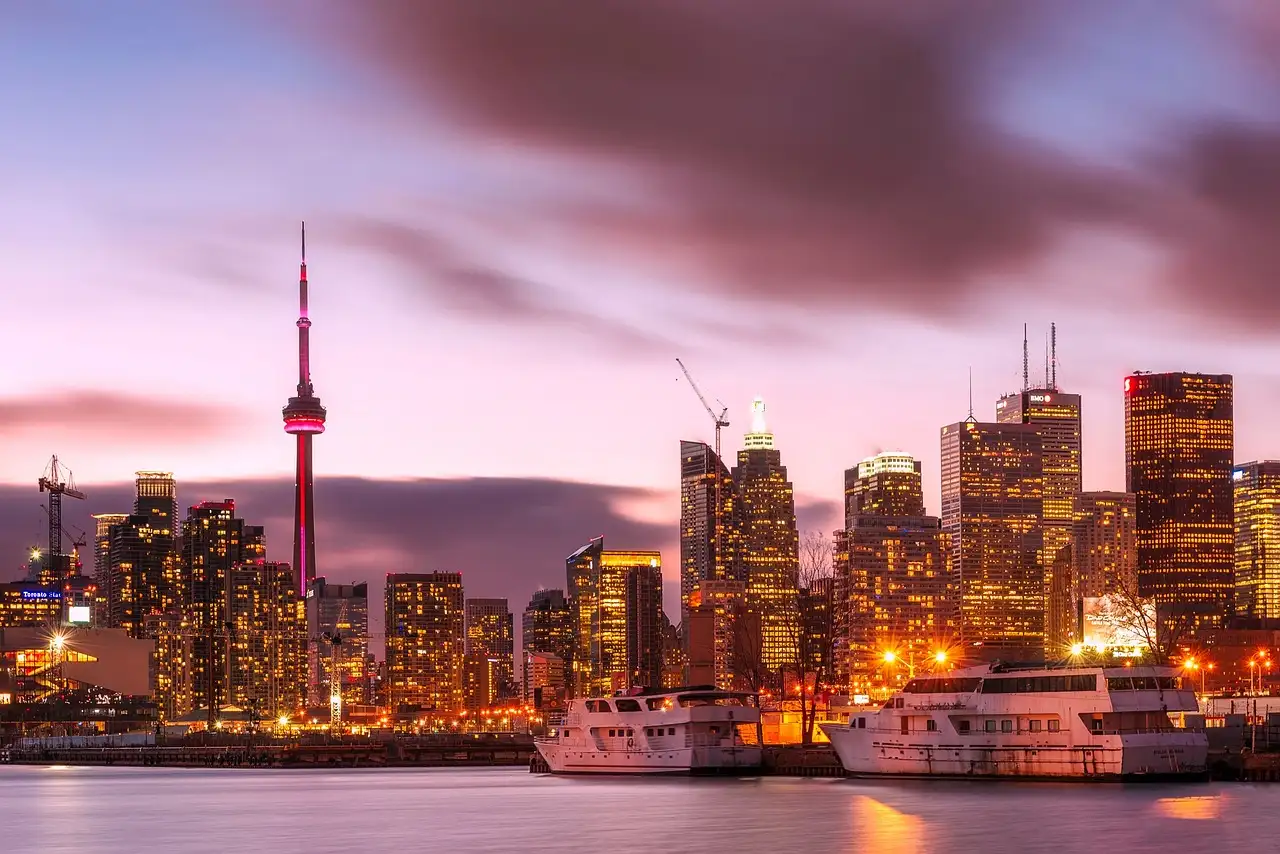 Der CN Tower und Downtown Toronto in der Dämmerung, mit zwei weißen Ausflugsbooten im Hafen
