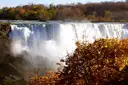 Die Niagarafälle werfen weiße Gischt auf, darüber ein Hang mit rotem und goldenem Herbstlaub.