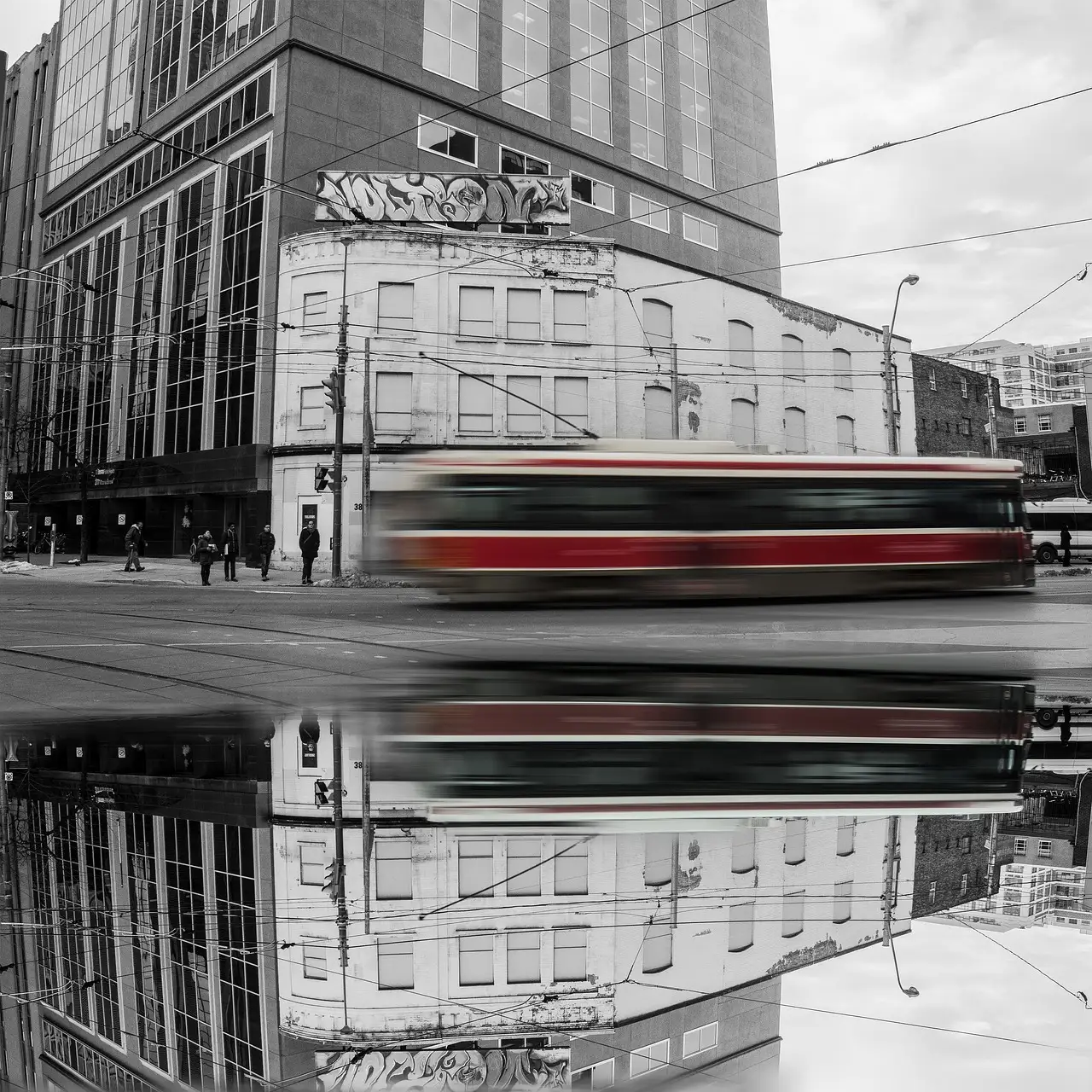 Eine rot-weiße Straßenbahn in Toronto fährt verwischt durch eine Straße in Downtown und spiegelt sich unten in einer Pfütze.