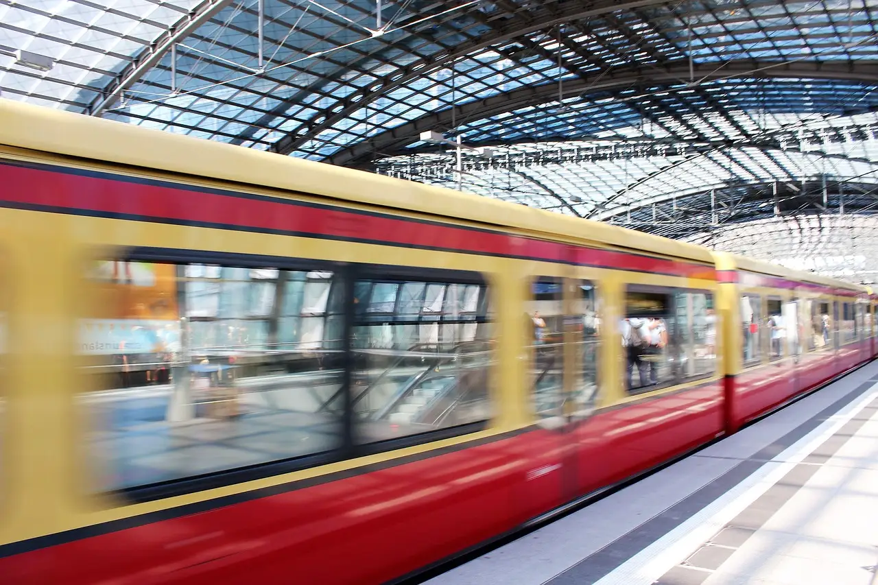 Un tren rojo y amarillo del S-Bahn de Berlín pasa a toda velocidad junto a un andén bajo el techo de cristal de la estación