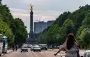 Una mujer va en bici hacia la Columna de la Victoria por una avenida ancha de Berlín con árboles y tráfico