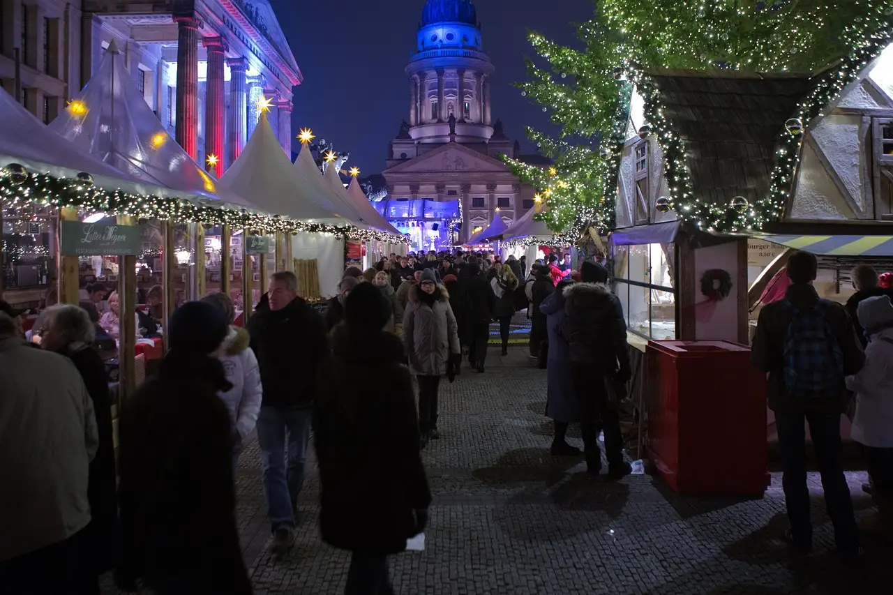 Gente paseando de noche entre los puestos iluminados del mercadillo navideño de Gendarmenmarkt, con una iglesia con cúpula al fondo