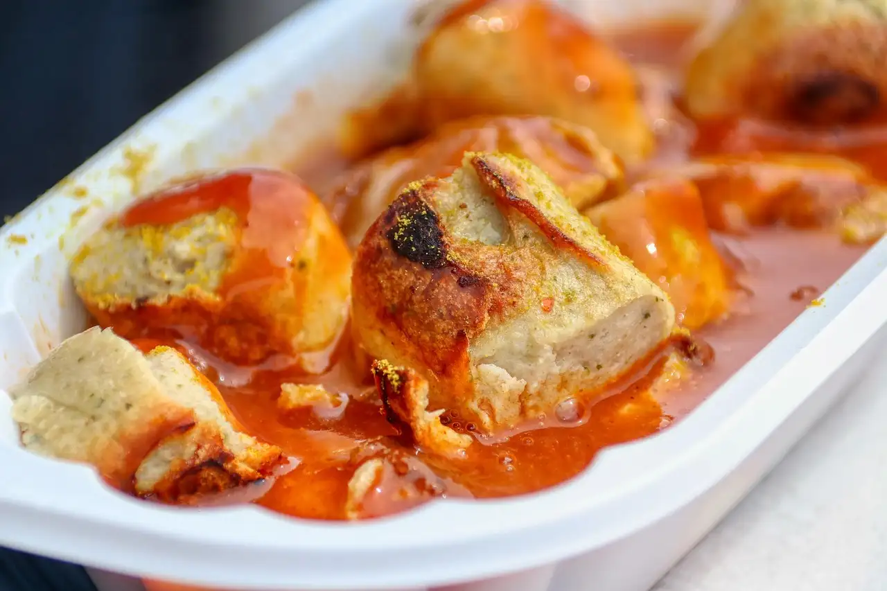 Primer plano de una currywurst en rodajas con salsa de kétchup al curry, servida en una bandeja de papel blanca