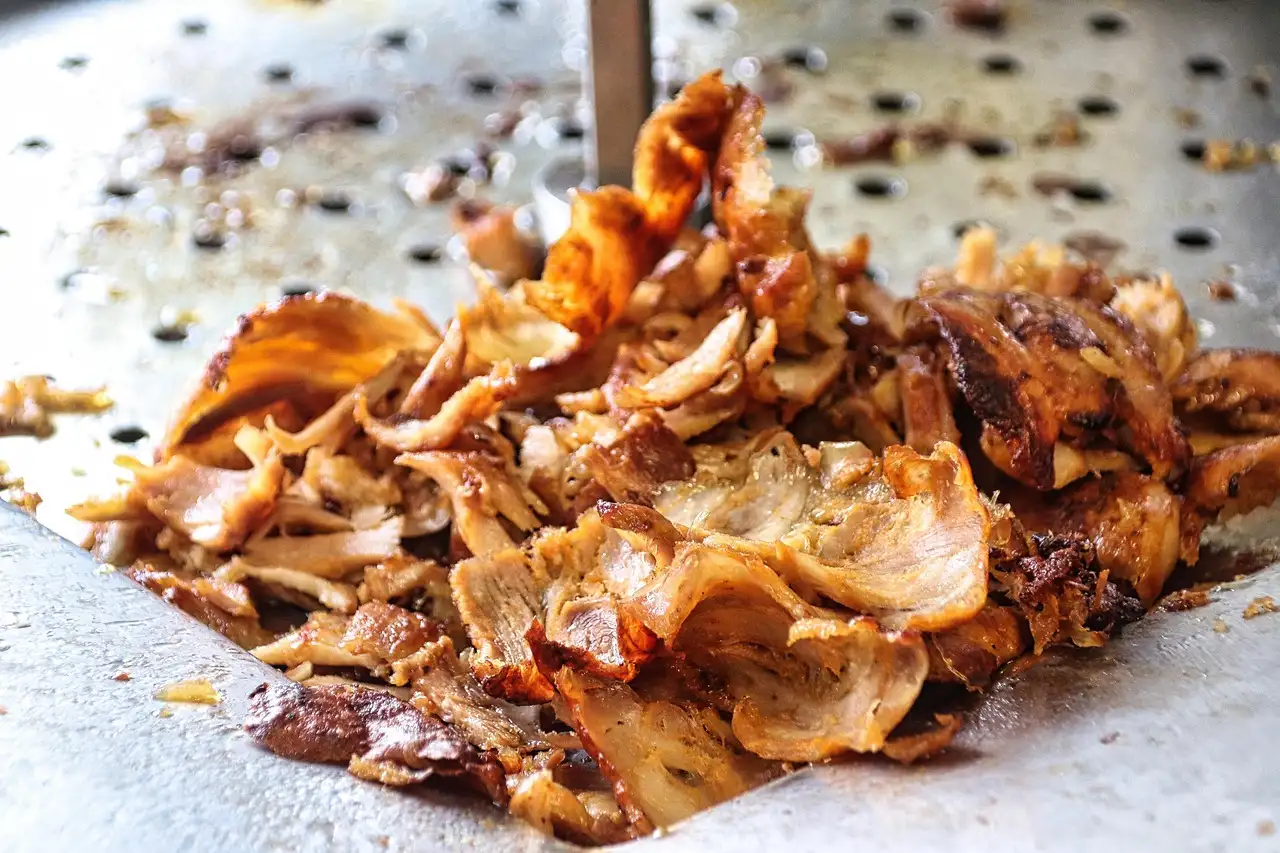 Carne de döner en tiras chisporroteando en una plancha de metal caliente