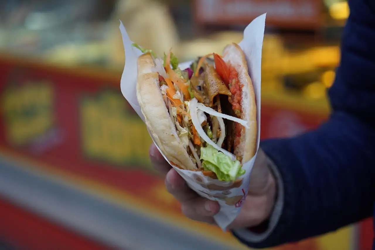 Una mano sujeta un döner kebab en pan de pita, envuelto en papel