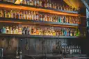 Un bar en penumbra con estanterías retroiluminadas llenas de botellas