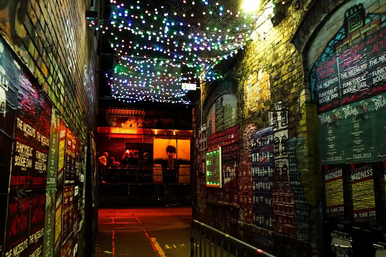 Un estrecho callejón entre patios de Berlín de noche, con guirnaldas de luces de colores y carteles en las paredes de ladrillo