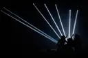 Haces de luz blanca atraviesan un club oscuro sobre las siluetas de la gente que baila