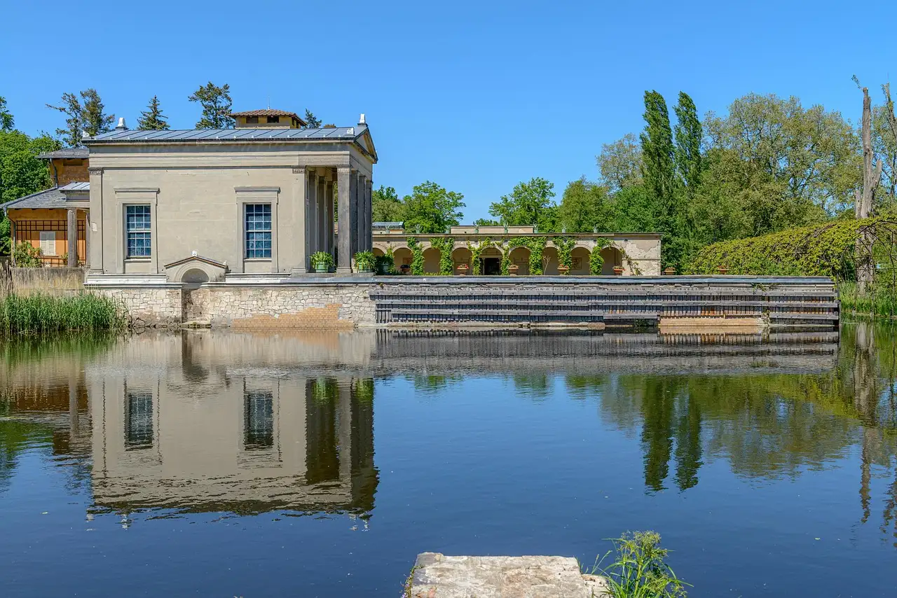 Un edificio clásico de jardín, de tono claro, reflejado en un estanque del parque de Sanssouci