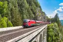 Un tren Railjet rojo de Austria cruza un viaducto de piedra entre laderas de montaña con bosque