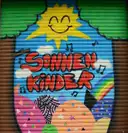 La persiana de una tienda pintada de colores, con un sol sonriente y las palabras Sonnen Kinder