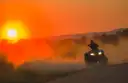 Un quad con los faros encendidos atraviesa el polvo bajo un cielo naranja de tarde