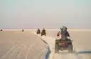 Pilotos en quads se alejan por la arena llana