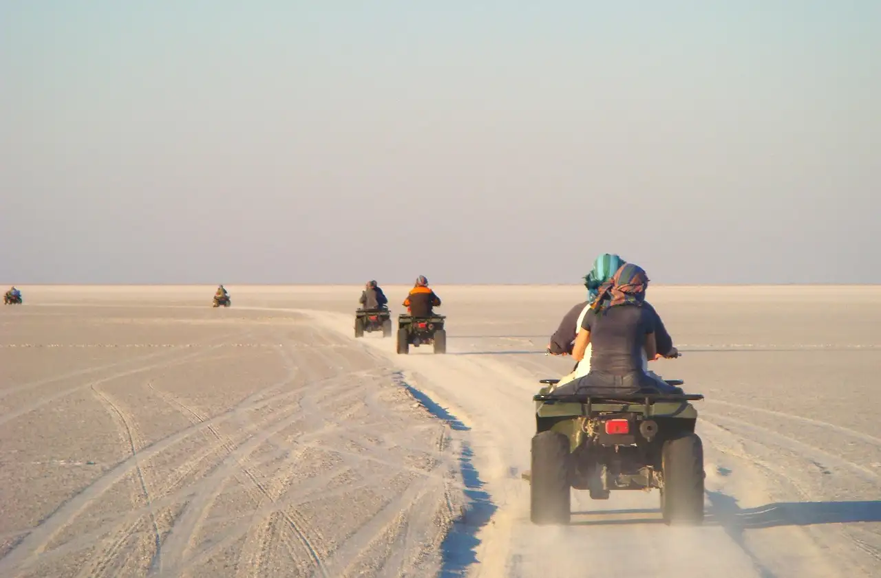 Pilotos en quads se alejan por la arena llana