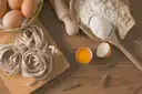 Nidos de tagliatelle frescos en una tabla de madera con huevos, harina y un rodillo