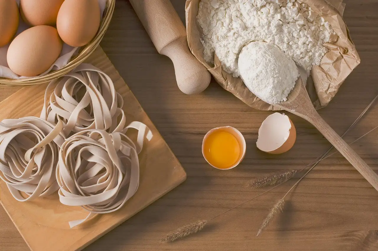 Nidos de tagliatelle frescos en una tabla de madera con huevos, harina y un rodillo