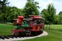 Un tren en miniatura rojo y verde lleva a niños por un parque verde de Houston