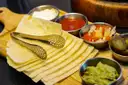 Tortillas calientes en una tabla con cuencos pequeños de salsa y guacamole