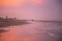 Un atardecer rosa y naranja sobre una amplia playa de Galveston, con hoteles a lo lejos en la orilla