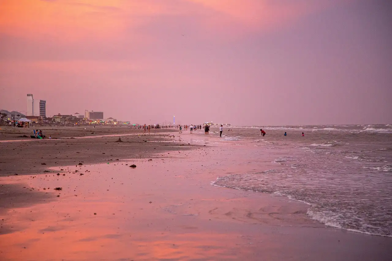 Un atardecer rosa y naranja sobre una amplia playa de Galveston, con hoteles a lo lejos en la orilla