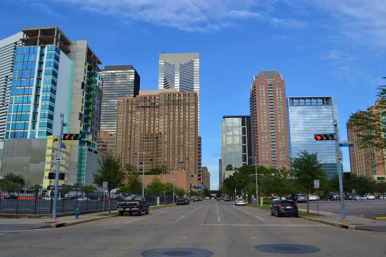 Una calle ancha del centro de Houston, flanqueada por torres de oficinas, bajo un cielo azul