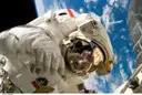 Un astronauta con traje espacial blanco durante un paseo espacial, con la Tierra y las nubes detrás (foto de la NASA, imagen genérica del espacio)