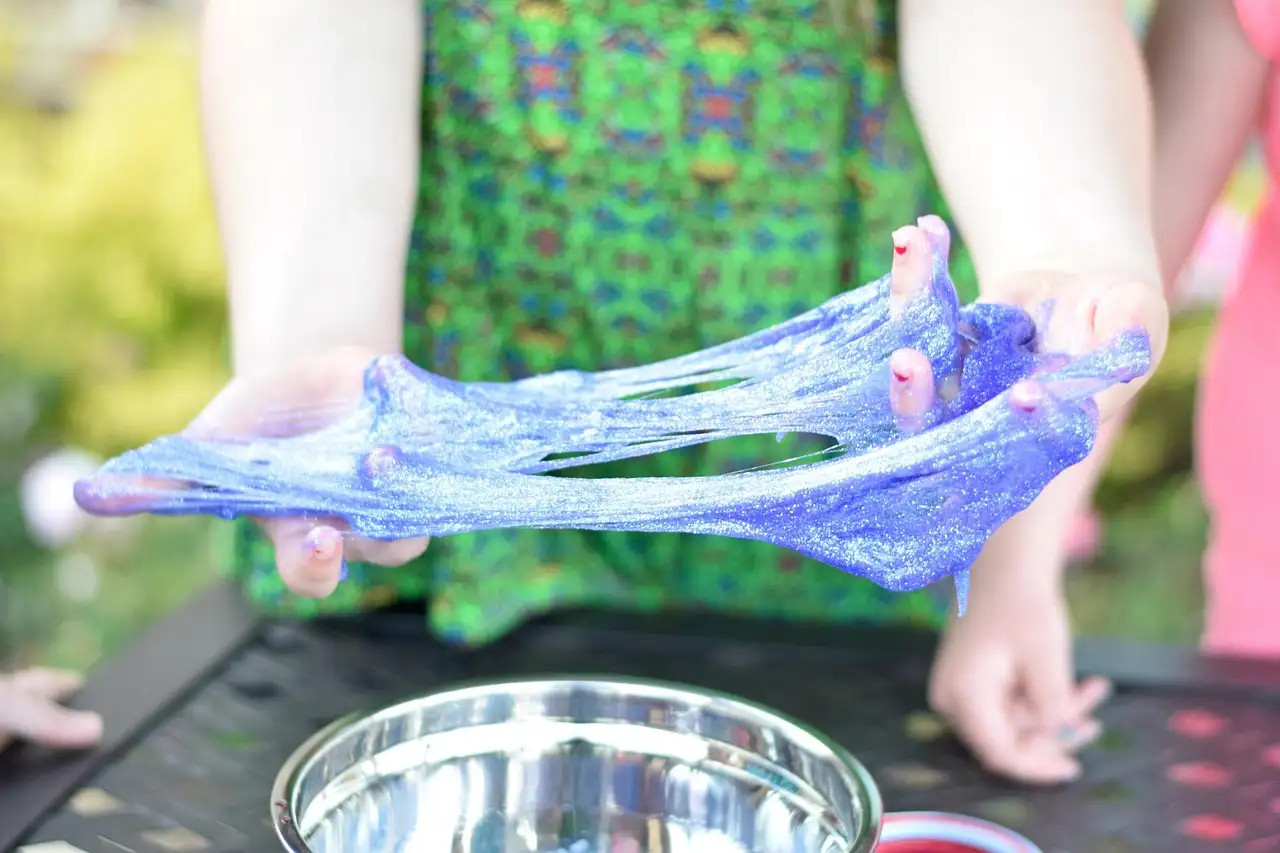 Dos manos estiran slime morado brillante sobre un cuenco metálico