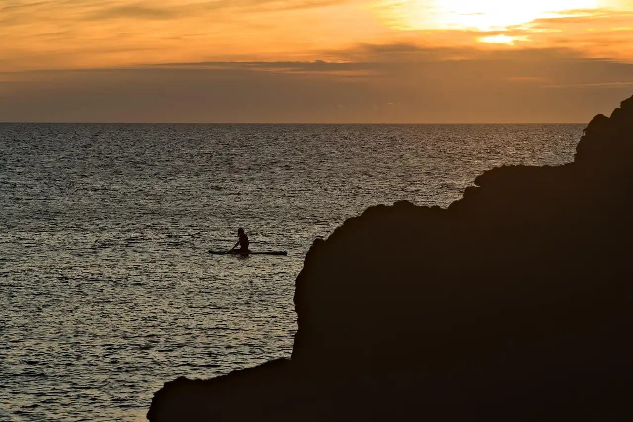 Un kayakista solitario en aguas abiertas bajo un atardecer naranja