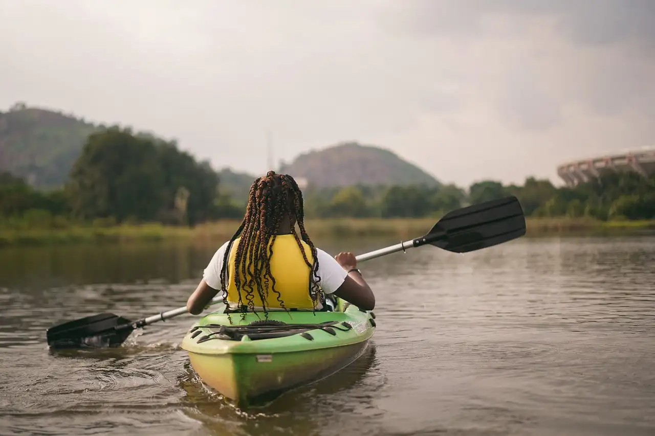 Un palista con chaleco salvavidas en un kayak verde sobre un río tranquilo