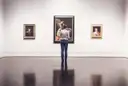 Un visitante mira cuadros antiguos en la pared blanca de una galería de arte