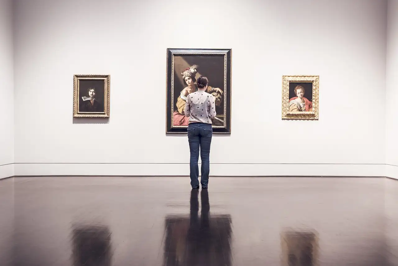Un visitante mira cuadros antiguos en la pared blanca de una galería de arte