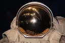 La visera dorada de un casco de astronauta sobre un traje espacial blanco, en primer plano