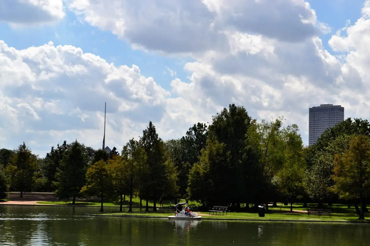 Una barca pequeña en el lago de Hermann Park, en Houston, con árboles y un edificio alto al fondo