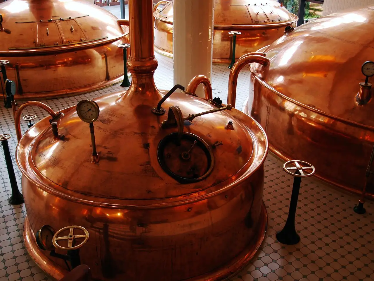 Grandes calderas de cobre para elaborar cerveza, con tuberías y manómetros, en una sala de cocción