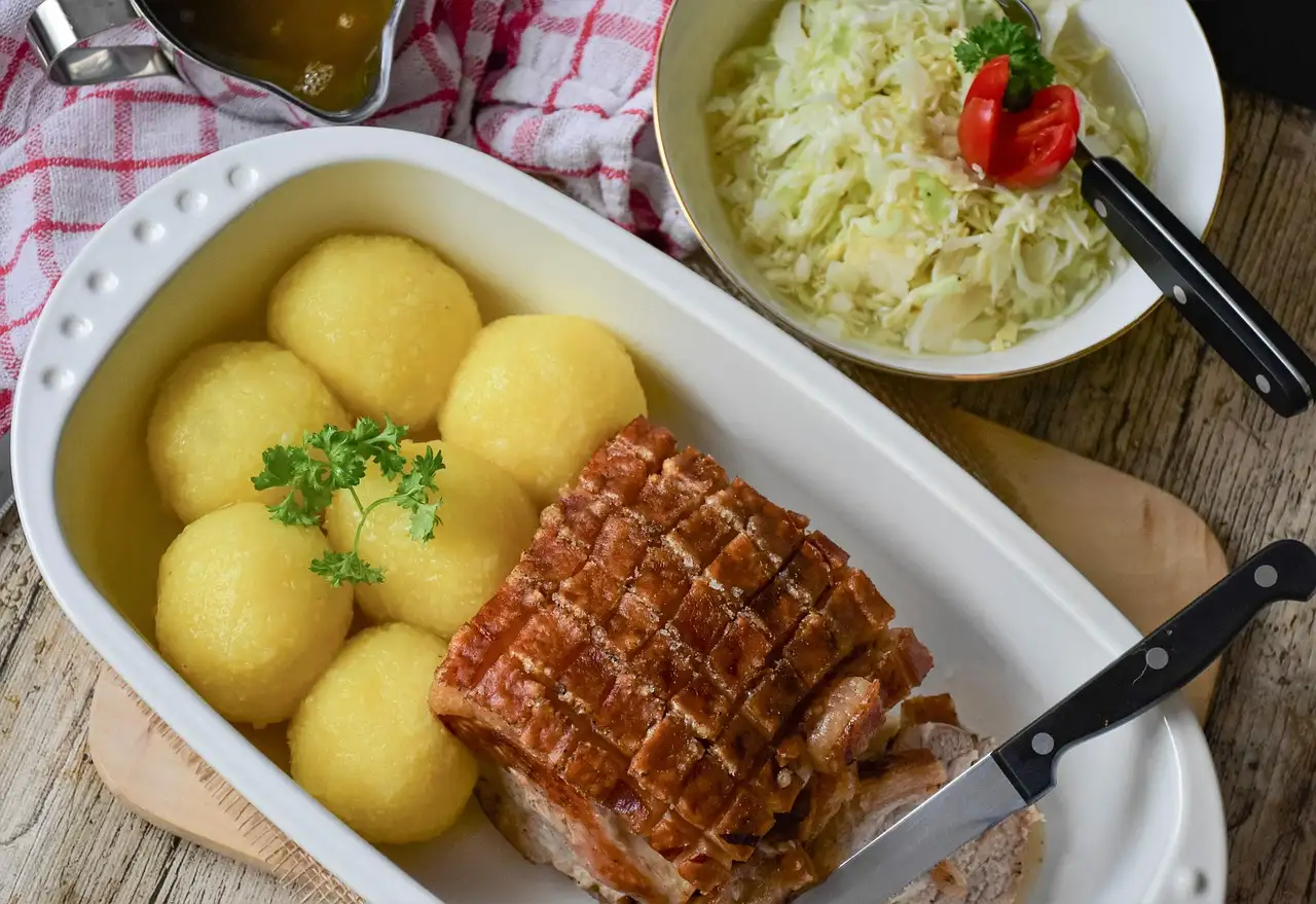 Asado de cerdo con albóndigas de patata y ensalada de col en una fuente blanca