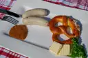 Dos salchichas blancas, un pretzel, mostaza dulce y mantequilla en un plato blanco