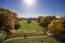 Caminos entre las amplias praderas otoñales del Jardín Inglés, con torres de Múnich en el horizonte