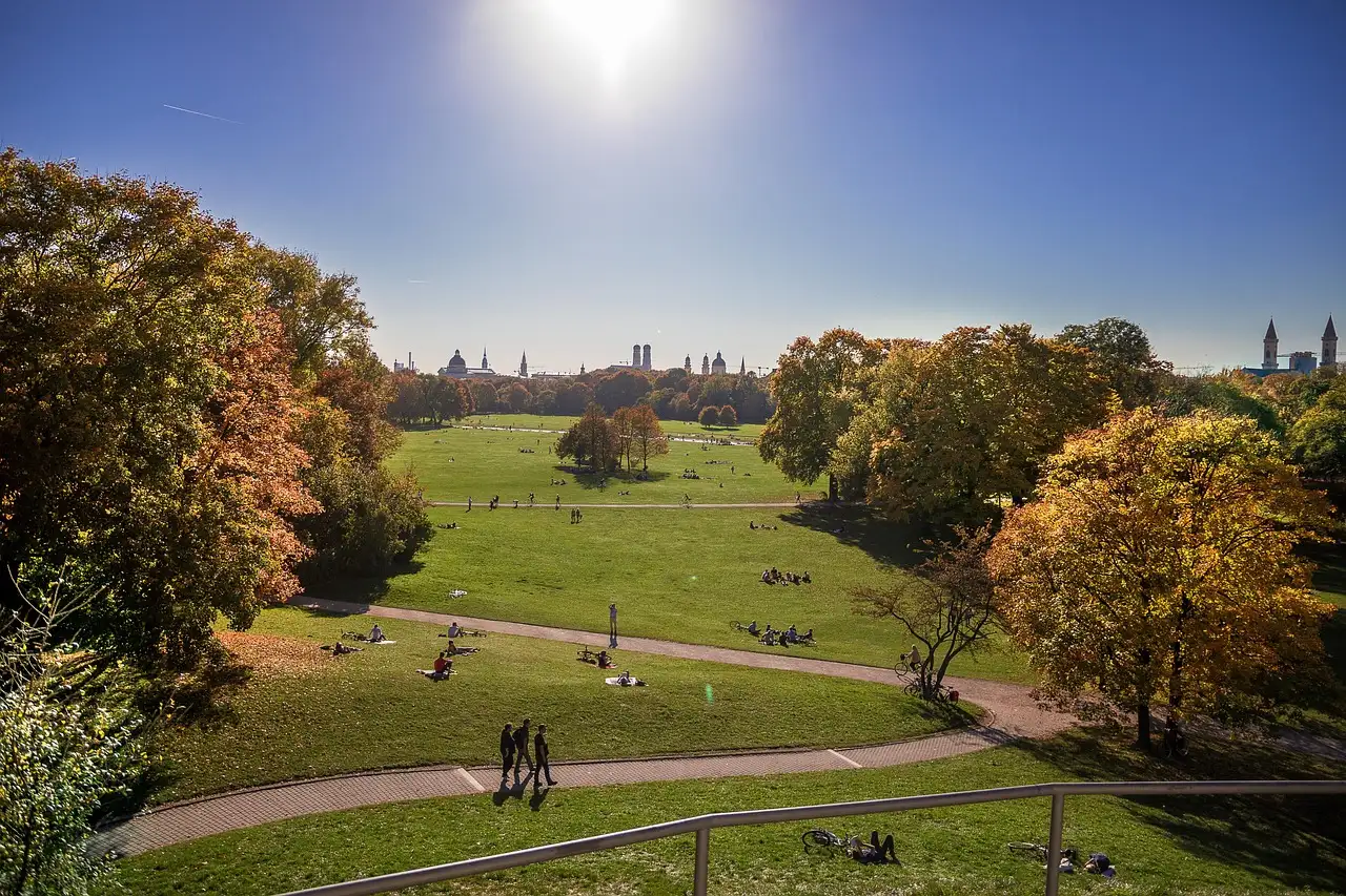 Caminos entre las amplias praderas otoñales del Jardín Inglés, con torres de Múnich en el horizonte