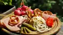 Una tabla de madera con jamón, pretzels, rábanos, aros de cebolla, pepinillos y tomates