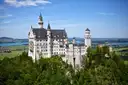El castillo de Neuschwanstein sobre un bosque verde, con lagos a lo lejos
