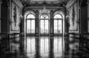 Una foto en blanco y negro de un salón de baile decorado, con ventanales y una lámpara de araña