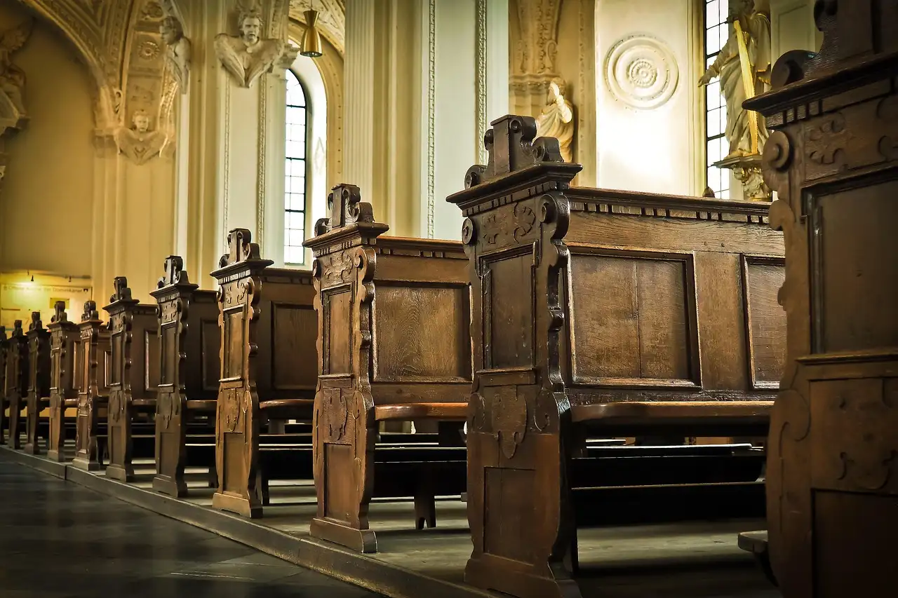 Bancos de madera tallada en una capilla antigua, iluminados por la luz de la ventana